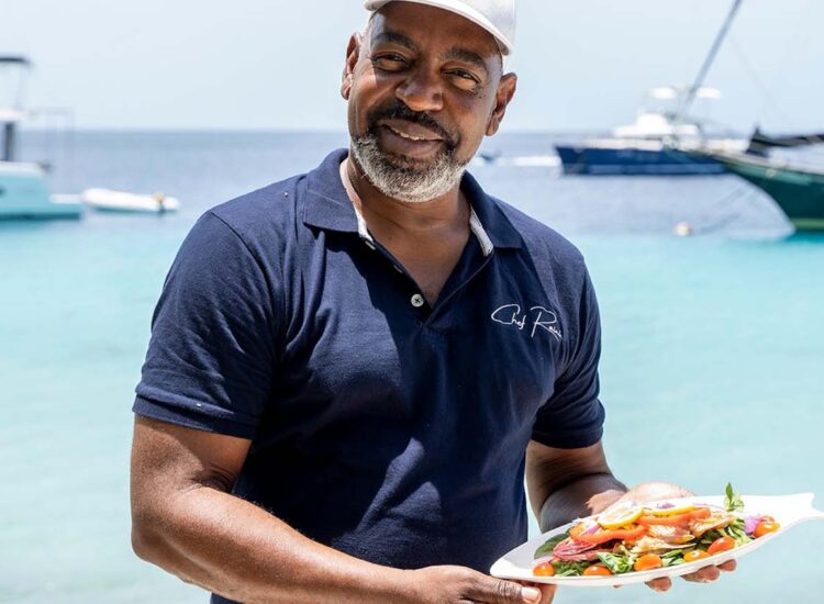 Man holding a plate of food with the ocean in the background