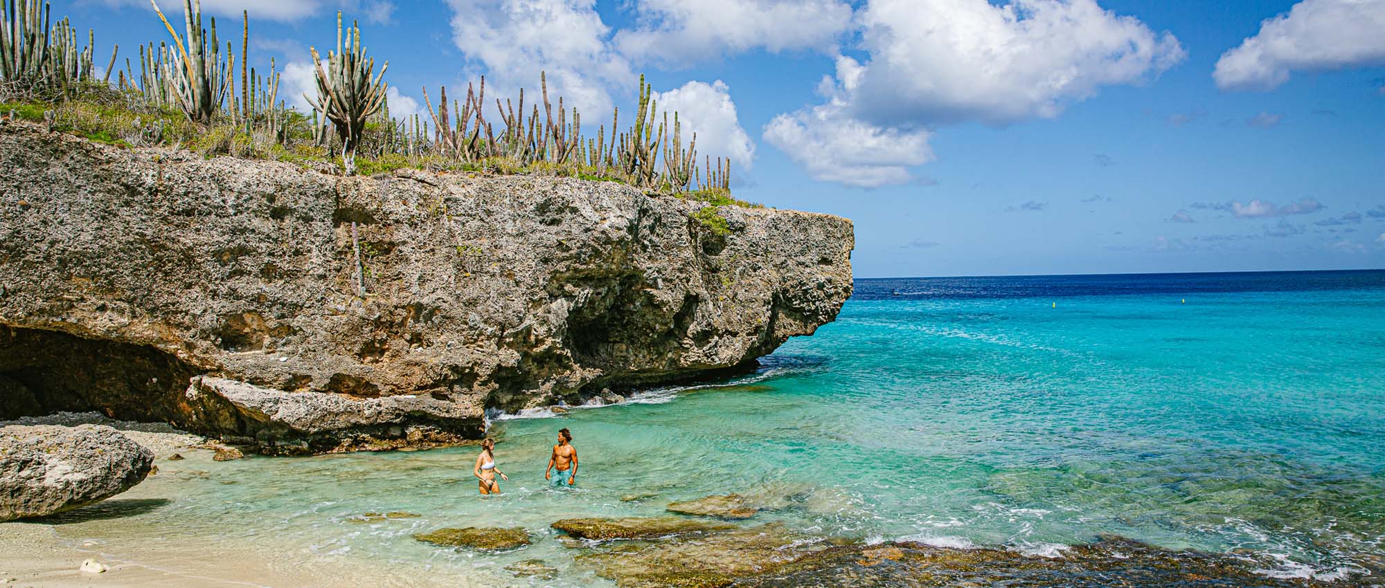 Male and female standing in ocean water surrounded by rocks